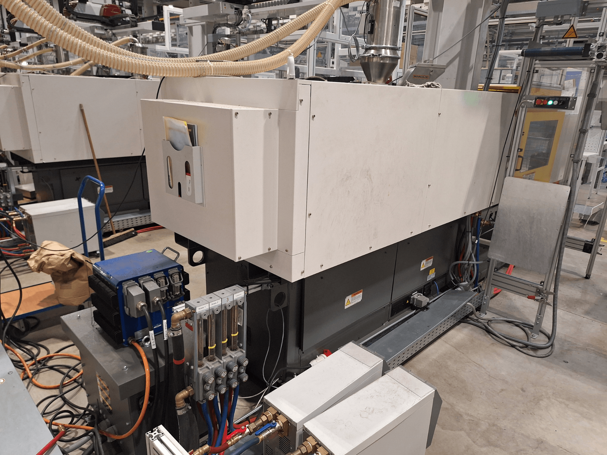 Tööstusseadmed tehases; sisaldab suurt masinat koos juhtpaneeli, voolikute ja elektriühendustega, külgvaade.