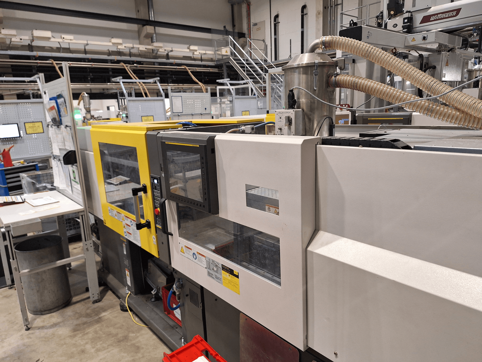 Mitmevärvilise, kollaste ja hallide sektsioonidega survevalu masina esivaade koos juhtpaneeli ja väljalaskesüsteemiga.