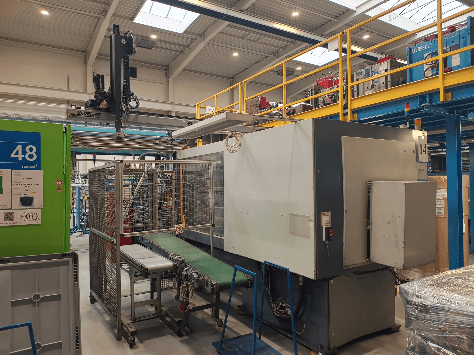 Tööstusautomaatikaseadmed rohelise konveieriga, millel on silt "48", ja kraana; masina külgvaade tehase põrandal.